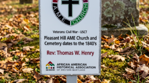 Historic cemetery marker for Pleasant Hill AME Church standing among fallen autumn leaves. The sign states that Pleasant Hill AME Church and Cemetery dates to the 1840s and recognizes Civil War veterans of the United States Colored Troops (USCT), including Rev. Thomas W. Henry. The marker features the logo of the African American Historical Association of Western Maryland.
